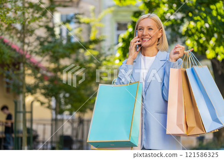 Happy mature businesswoman lady smiling laughs standing on city street holding shopping packages Happy mature businesswoman lady smiling laughs standing on city street holding shopping packages 121586325