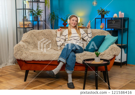 Caucasian woman enjoying relaxing on sofa listening to music with headphones holding smartphone 121586416