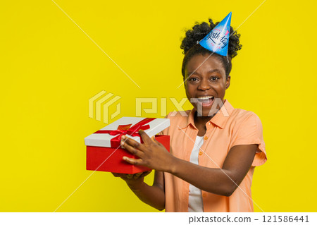 African American woman opening present gift box, party hat, birthday surprise, joyful reaction African American woman opening present gift box, party hat, birthday surprise, joyful reaction 121586441