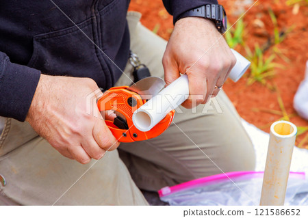 Worker uses hand tool to cut PVC pipe while working at home improvement on water well system Worker uses hand tool to cut PVC pipe while working at home improvement on water well system 121586652