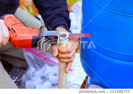Contractor uses power hand saw to cut pipe for constructing water storage system during plumbing water line installation 121586757