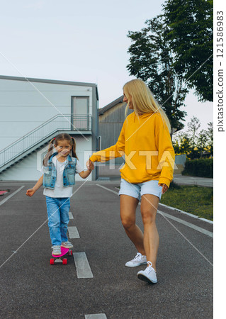 Mom helping her daughter to put on a helmet and ride a skateboard Mom helping her daughter to put on a helmet and ride a skateboard 121586983