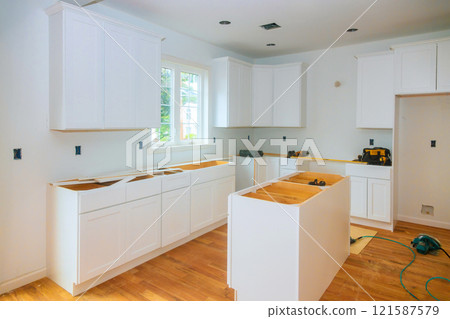 Cabinets are being installed in spacious kitchen filled with natural light during home renovation project 121587579