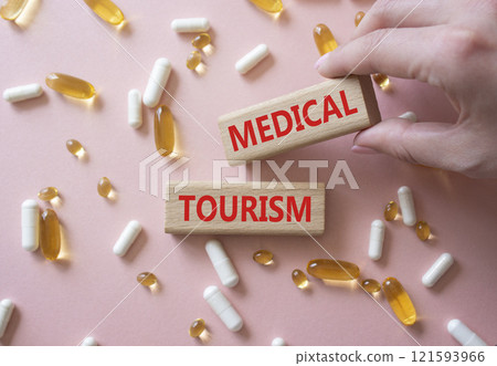 Medical Tourism symbol. Concept word Medical Tourism on wooden blocks. Beautiful pink background with pills. Doctor Hand. Medicine and Medical Tourism concept. Copy space 121593966