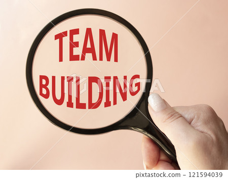 Team Building symbol. Concept word Team Building on magnifying glass. Businessman hand. Beautiful pink background. Business and Team Building concept. Copy space Team Building symbol. Concept word Team Building on magnifying glass. Businessman hand. Beautiful pink background. Business and Team Building concept. Copy space 121594039