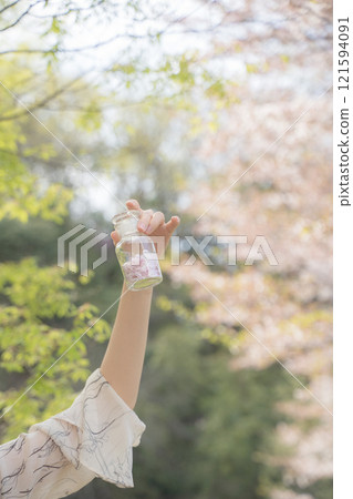 Woman holding a bottle of cherry blossom petals under the cherry blossoms Woman holding a bottle of cherry blossom petals under the cherry blossoms 121594091