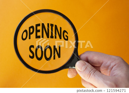 Opening soon symbol. Magnifying Glass with Concept word Opening soon. Beautiful orange background. Businessman hand. Business and Opening soon concept. Copy space Opening soon symbol. Magnifying Glass with Concept word Opening soon. Beautiful orange background. Businessman hand. Business and Opening soon concept. Copy space 121594271