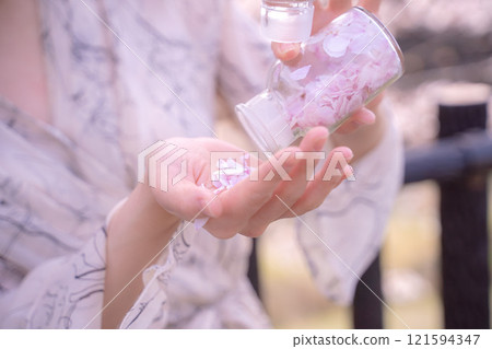 一個女人的手拿著一個裝滿櫻花花瓣的瓶子 121594347