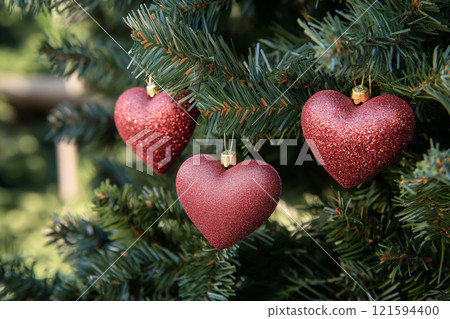 Close-up of red heart-shaped ornaments on a Christmas tree with festive lights. Christmas balls in a shape of a heart. Love and romantic symbol, Saint Valentine's Day background 121594400