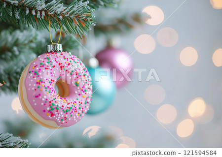 Decorative Pink Doughnut Ornament Hanging on Christmas Tree with Festive Lights. Diet, fasting and new beginning concept. New Year resolutions 121594584