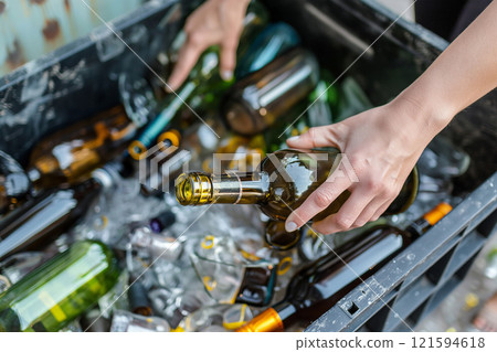 Hands sorting glass bottles into a recycling bin. Environmental responsibility and sustainable practices. The image highlights waste management and the importance of a clean, eco-friendly environment. 121594618