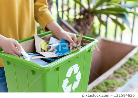 Woman sorting recyclable papers into a colorful recycling bin outdoors. Eco-friendly behavior, sustainable practices, and environmental care, responsibility and conservation 121594626
