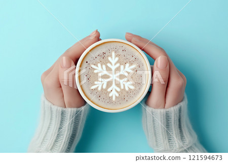 Hands in white sweater cuffs holding a cup of coffee or cocoa with a snowflake latte art on its foam, evoking winter themes, comfort, and coziness during cold seasons. Coffee lovers concept 121594673