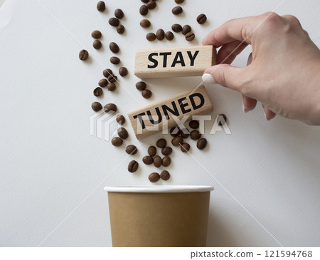 Stay Tuned symbol. Concept word Stay Tuned on wooden blocks. Businessman hand. Beautiful white background with coffee cup. Business and Stay Tuned concept. Copy space 121594768