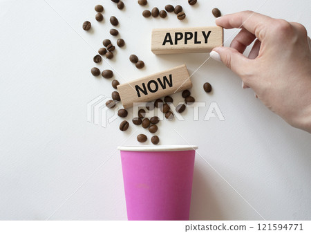 Apply now symbol. Concept word Apply now on wooden blocks. Beautiful white background with coffee cup. Businessman hand. Business and Apply now concept. Copy space 121594771