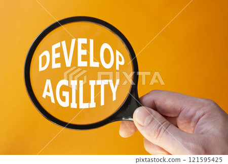 Develop agility symbol. Concept word Develop agility on magnifying glass. Beautiful orange background. Businessman hand. Business and Develop agility concept. Copy space 121595425