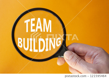 Team Building symbol. Concept word Team Building on magnifying glass. Businessman hand. Beautiful orange background. Business and Team Building concept. Copy space Team Building symbol. Concept word Team Building on magnifying glass. Businessman hand. Beautiful orange background. Business and Team Building concept. Copy space 121595464