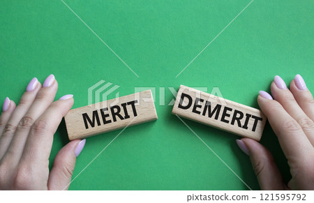 Merit or Demerit symbol. Concept word Merit or Demerit on wooden blocks. Businessman hand. Beautiful green background. Business and Merit or Demerit concept. Copy space Merit or Demerit symbol. Concept word Merit or Demerit on wooden blocks. Businessman hand. Beautiful green background. Business and Merit or Demerit concept. Copy space 121595792