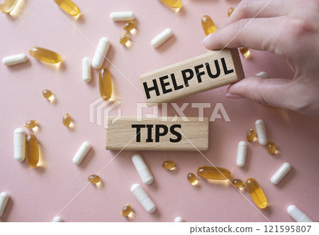 Helpful tips symbol. Concept word Helpful tips on wooden blocks. Doctor Hand. Beautiful pink background with pills. Medicine and Helpful tips concept. Copy space 121595807