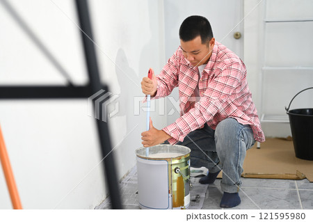 Man preparing for a painting project mixing paint in a can with stirring stick 121595980