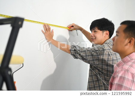 Two young men measuring a wall preparing for a home improvement project 121595992