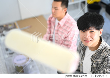 Two young asian men painting walls with a roller brush during renovation 121595995