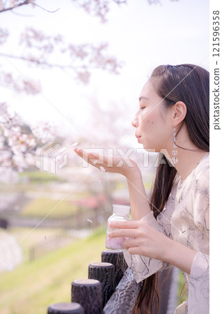 A cute woman blowing cherry blossom petals and playing with them 121596358