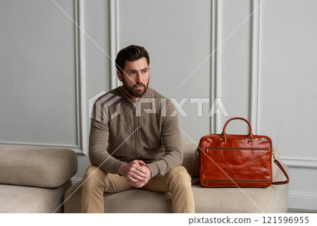 A man is comfortably sitting on a sofa, with a leather orange briefcase 121596955