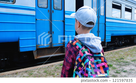A 9-year-old boy with a backpack on his shoulders stands on a railway platform and looks at a train A 9-year-old boy with a backpack on his shoulders stands on a railway platform and looks at a train 121597835