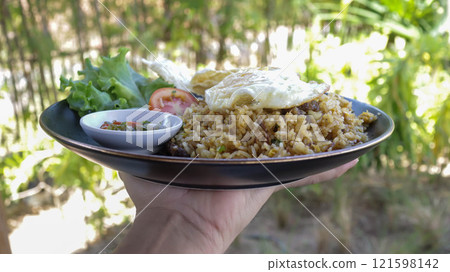 A hand holding or carry a plate of fried rice with nature background. 121598142