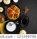 Cinnabon cinnamon rolls buns with pumpkin in black pan and cup of tea and empty plate on black background. Top view. Sweet Homemade Pastry autumn baking. Close-up, copy space 121599796