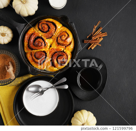 Cinnabon cinnamon rolls buns with pumpkin in black pan and cup of tea and empty plate on black background. Top view. Sweet Homemade Pastry autumn baking. Close-up, copy space Cinnabon cinnamon rolls buns with pumpkin in black pan and cup of tea and empty plate on black background. Top view. Sweet Homemade Pastry autumn baking. Close-up, copy space 121599796