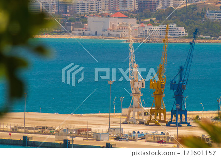 Harbour cranes against the background of the blue sea with slightly blurred contours due to the heat and warm air currents in the air. Concept of cargo transportation by sea Harbour cranes against the background of the blue sea with slightly blurred contours due to the heat and warm air currents in the air. Concept of cargo transportation by sea 121601157