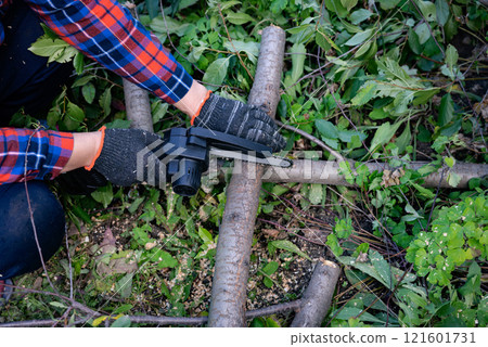 A man in gloves saws a wooden tree trunk with a saw. Gardening work. A man in gloves saws a wooden tree trunk with a saw. Gardening work. 121601731