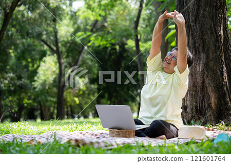 Happy Asian senior woman using laptop for working online outside office. Elderly retirement using laptop for learning new skill and freelance working in park, senior lifestyle with technology 121601764