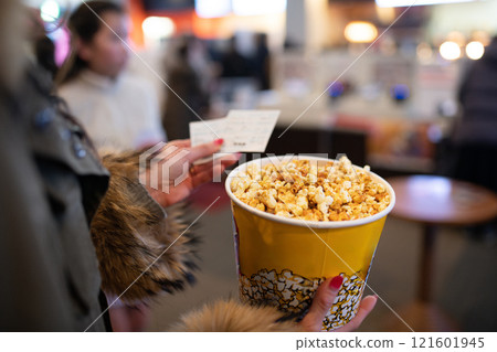 Woman holding popcorn and movie ticket stub 121601945