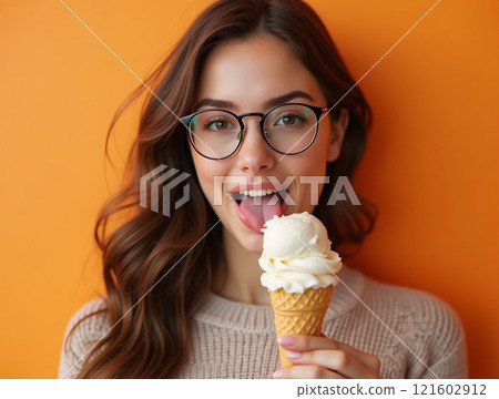 Young woman enjoying ice cream against a colorful orange background on a warm sunny day 121602912