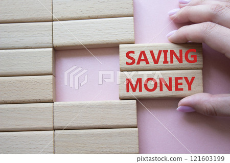 Saving Money symbol. Concept word Saving Money on wooden blocks. Businessman hand. Beautiful pink background. Business and Saving Money concept. Copy space Saving Money symbol. Concept word Saving Money on wooden blocks. Businessman hand. Beautiful pink background. Business and Saving Money concept. Copy space 121603199