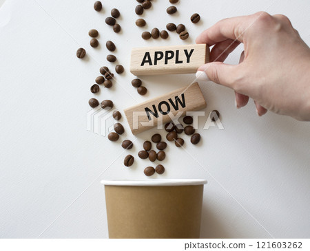 Apply now symbol. Concept word Apply now on wooden blocks. Beautiful white background with coffee cup. Businessman hand. Business and Apply now concept. Copy space 121603262