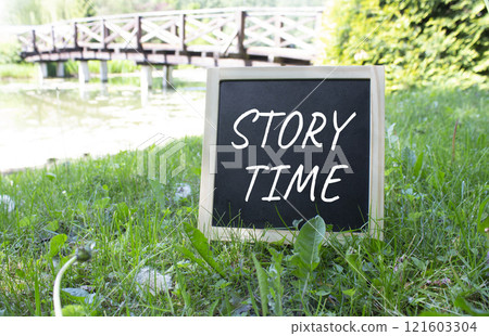 Story Time symbol. Concept word Story Time on black chalk background. Beautiful meadow background with bridge. Business and Story Time concept. Copy space Story Time symbol. Concept word Story Time on black chalk background. Beautiful meadow background with bridge. Business and Story Time concept. Copy space 121603304