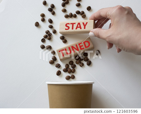 Stay Tuned symbol. Concept word Stay Tuned on wooden blocks. Businessman hand. Beautiful white background with coffee cup. Business and Stay Tuned concept. Copy space 121603596