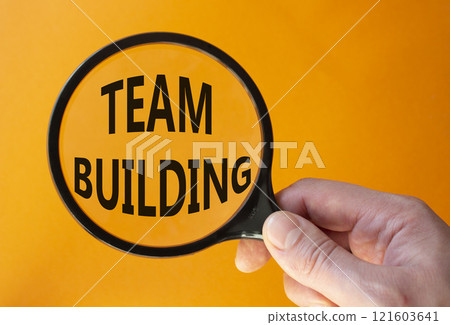 Team Building symbol. Concept word Team Building on magnifying glass. Businessman hand. Beautiful orange background. Business and Team Building concept. Copy space Team Building symbol. Concept word Team Building on magnifying glass. Businessman hand. Beautiful orange background. Business and Team Building concept. Copy space 121603641