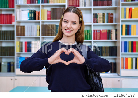 Happy teenage girl student showing heart gesture inside school building 121604188