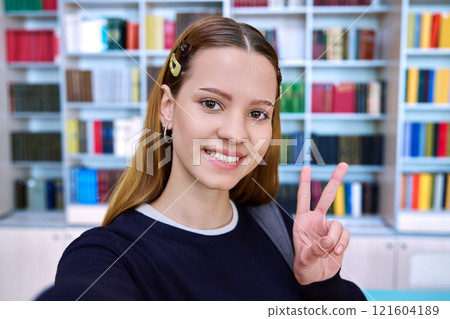 Selfie portrait of high school student girl showing hand gesture for victory, inside library Selfie portrait of high school student girl showing hand gesture for victory, inside library 121604189