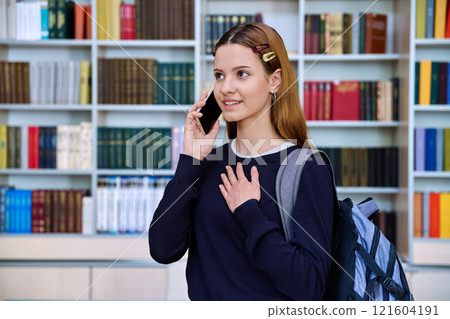 Teenage girl talking on mobile phone, inside high school building, in library Teenage girl talking on mobile phone, inside high school building, in library 121604191