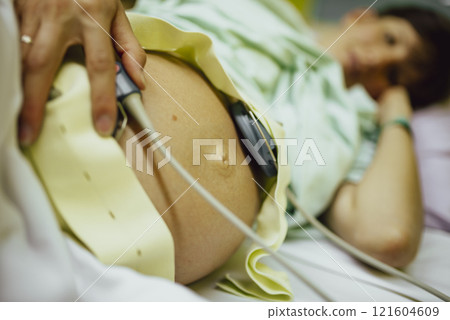 Pregnant woman lying in a hospital bed with baby heartbeat monitor on her belly 121604609