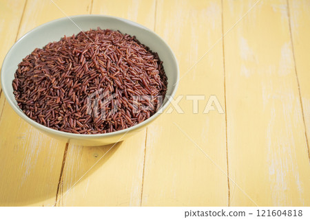 A bowl of red raw rice is placed on a yellow wooden table 121604818