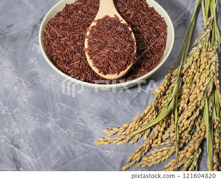 Beautiful red-rice in a bowl with spoon and ears of rice on wood 121604820