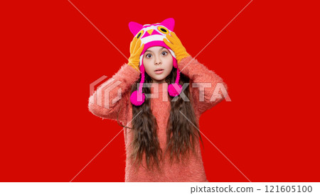 Teen kid girl wearing warm knitted winter earflap hat and sweater isolated on red 121605100