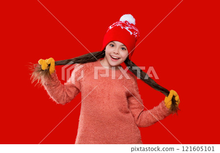 Teen kid girl wearing warm knitted winter earflap hat and sweater isolated on red 121605101